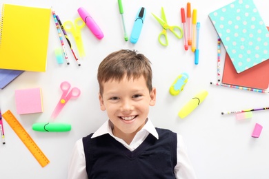 Photo of Cute child surrounded by school stationery on white background