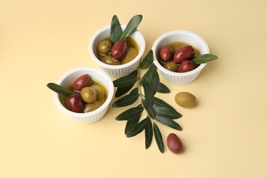 Bowls with different ripe olives and leaves on beige background