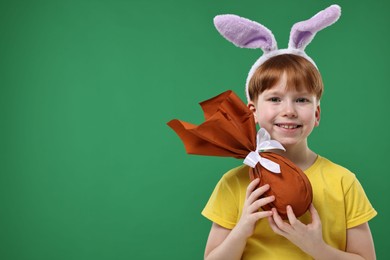 Photo of Easter celebration. Cute little boy with bunny ears and wrapped egg on green background. Space for text