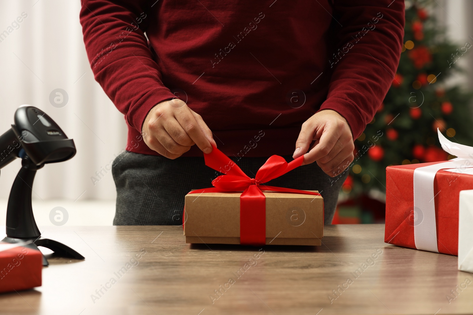 Photo of Man preparing Christmas gift box at wooden table in post office, closeup