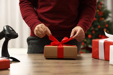 Photo of Man preparing Christmas gift box at wooden table in post office, closeup