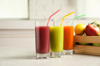 Three glasses of juices and wooden crate with fresh ingredients on light table. Space for text