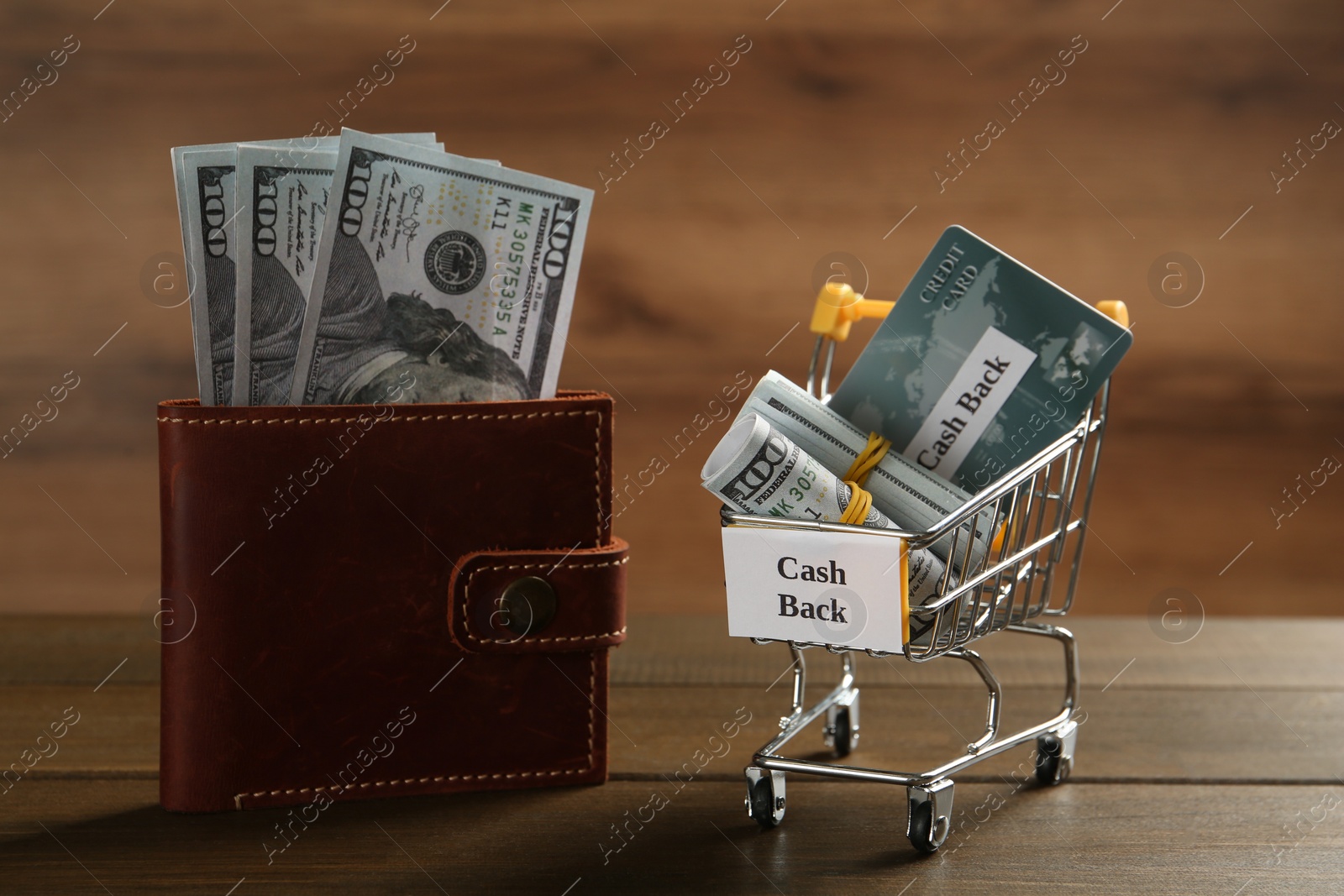 Photo of Small shopping cart with credit card, rolled banknotes and sign Cash Back near wallet on wooden table