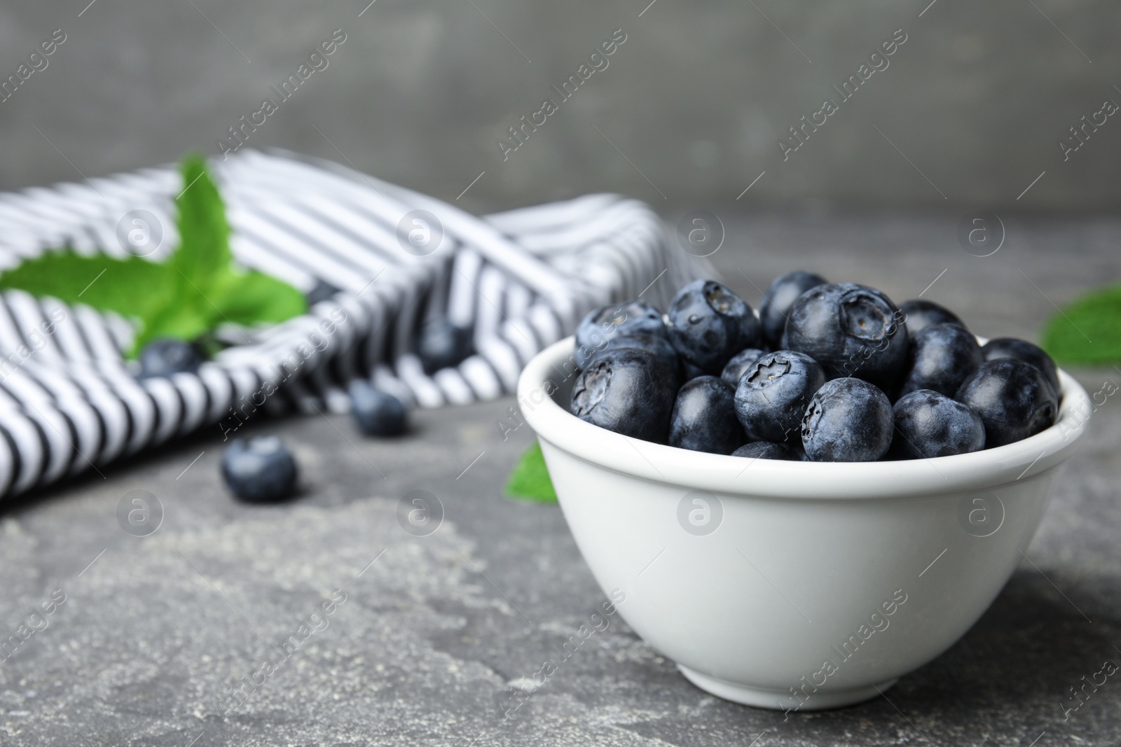 Photo of Bowl of tasty blueberries on grey stone surface, space for text