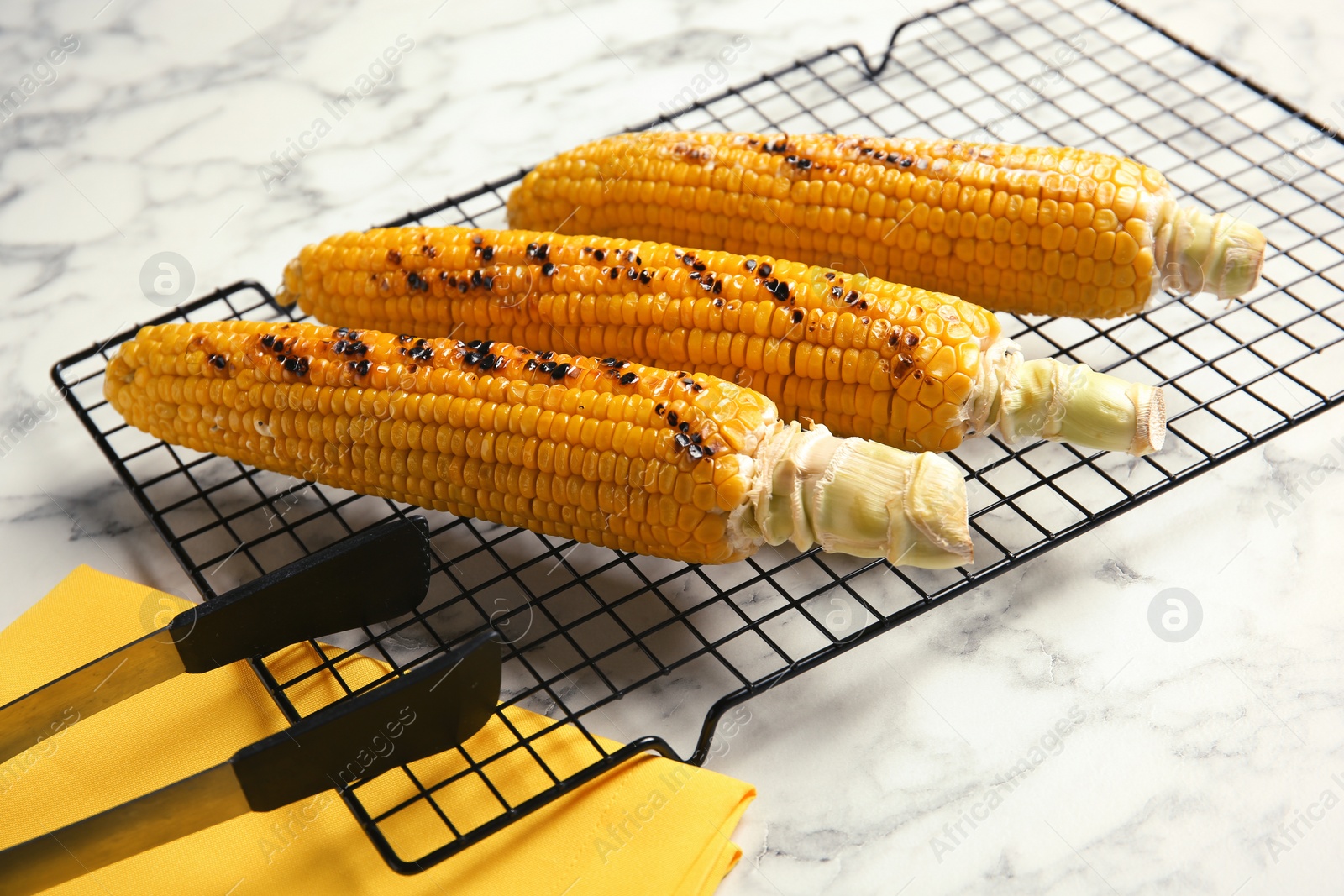 Photo of Cooling rack with grilled corn cobs on marble background