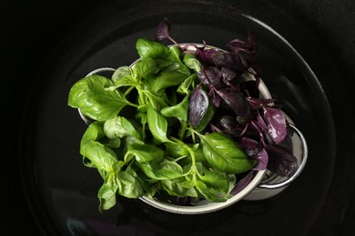 Photo of Metal colander of different fresh wet basil leaves in sink, top view