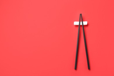 Photo of Pair of black chopsticks with rest on red background, top view. Space for text