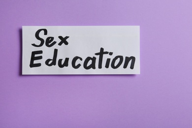 Photo of Piece of paper with phrase "SEX EDUCATION" on violet background, top view