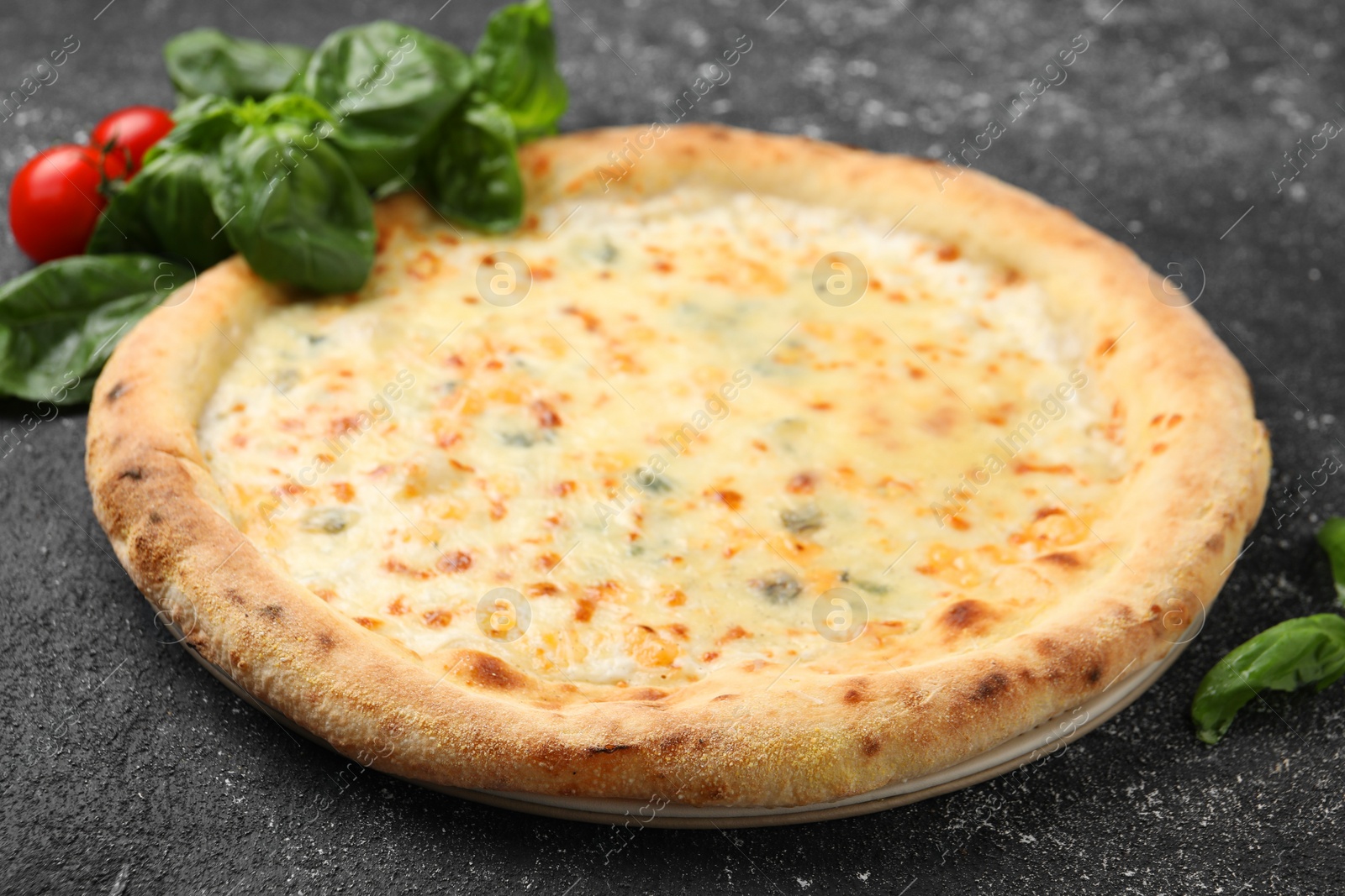 Photo of Delicious cheese pizza, basil and tomatoes on black textured table, closeup