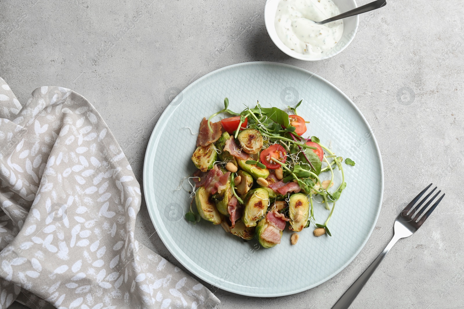 Photo of Delicious roasted Brussels sprouts with bacon served on light grey table, flat lay