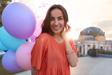 Cheerful young woman with color balloons outdoors on sunny day