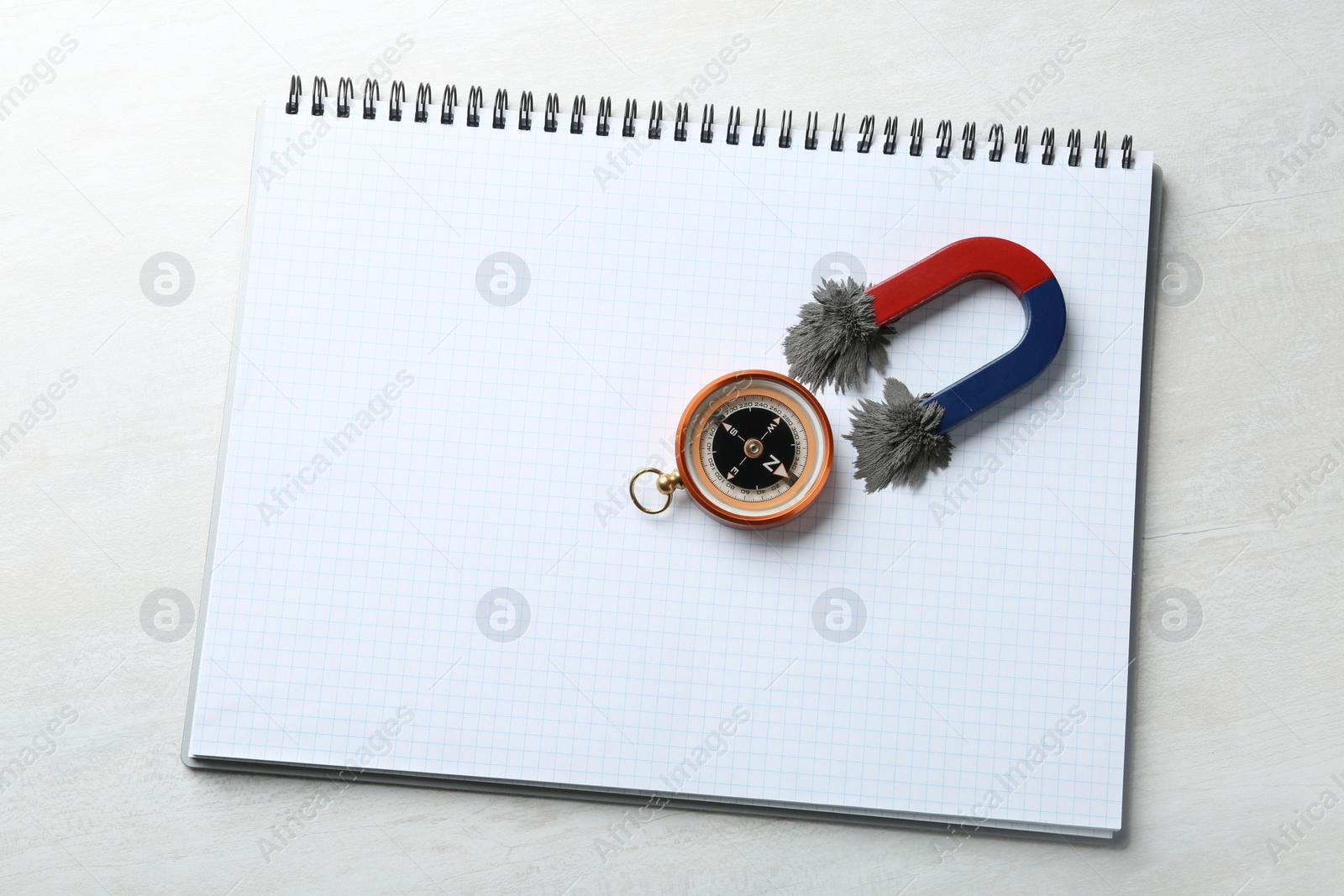 Photo of Notebook, compass and magnet with iron powder on light background, top view. Space for text