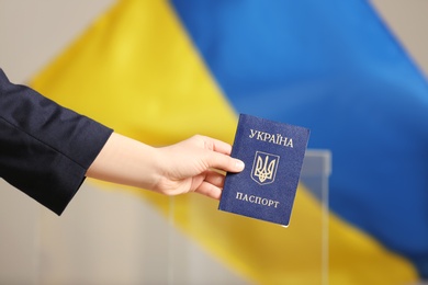 Woman holding Ukrainian internal passport against national flag at polling station, closeup