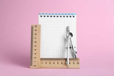 Photo of Rulers, notebook and compass on pink background