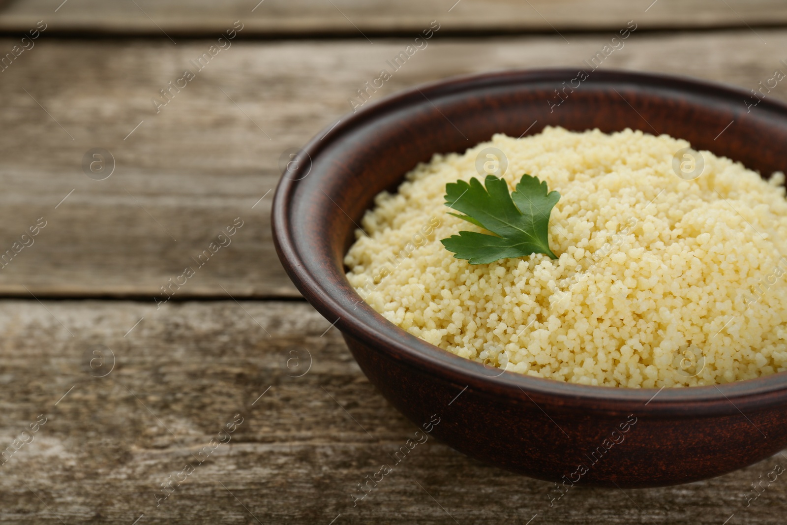 Photo of Tasty couscous with parsley on wooden table, closeup. Space for text