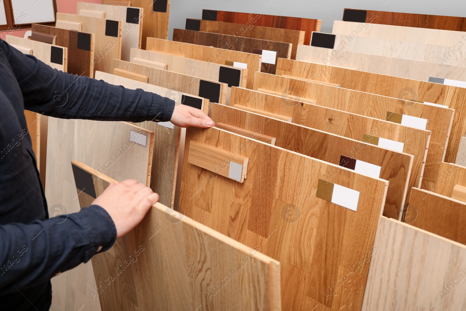 Photo of Man choosing wooden flooring among different samples in shop, closeup