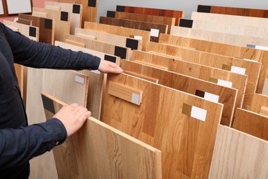 Photo of Man choosing wooden flooring among different samples in shop, closeup