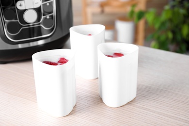 Cups with homemade yogurt near multi cooker on table in kitchen