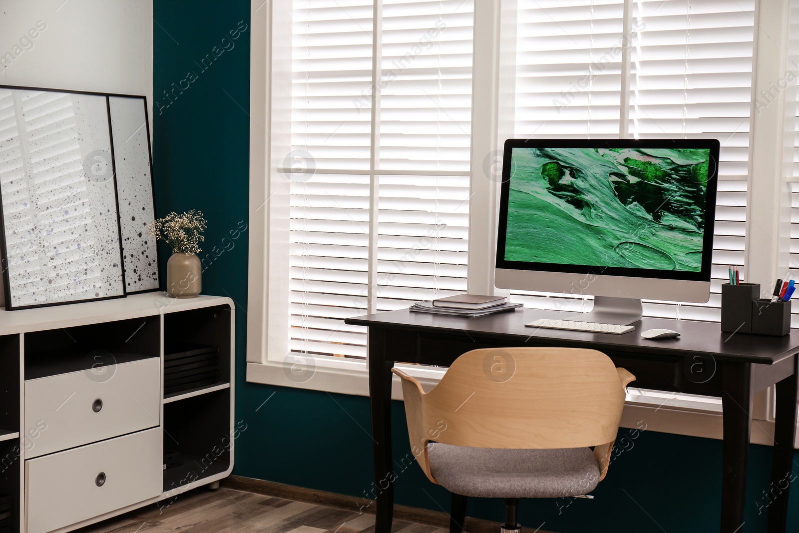 Photo of Comfortable workplace near window with white horizontal blinds in room