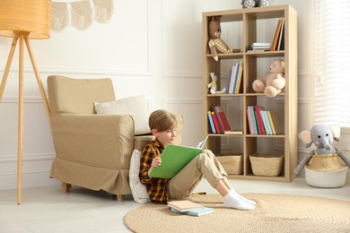 Photo of Little boy reading book on floor at home