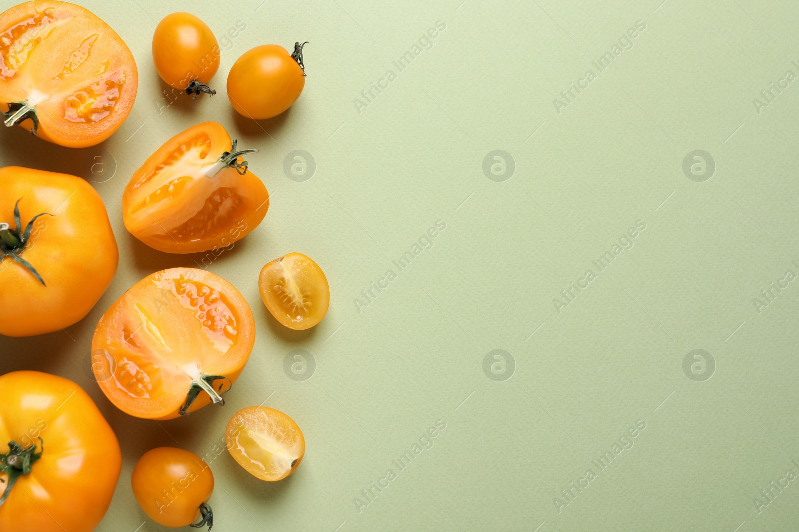 Photo of Cut and whole ripe yellow tomatoes on light green background, flat lay. Space for text