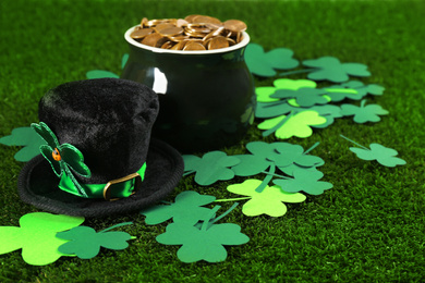 Photo of Hat, pot of gold coins and clover leaves on green grass. St. Patrick's Day celebration