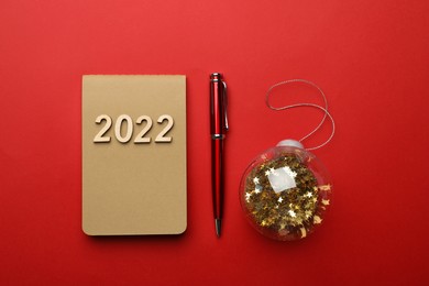 Photo of Stylish planner, pen and Christmas ball on red background, flat lay. Planning for 2022 New Year