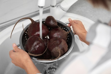 Photo of Woman washing ripe beets in kitchen sink, closeup