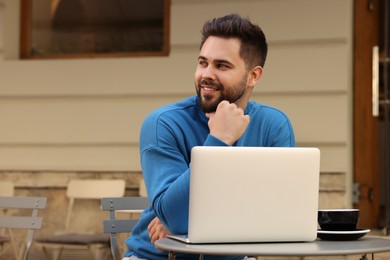 Handsome young man with laptop at table in outdoor cafe