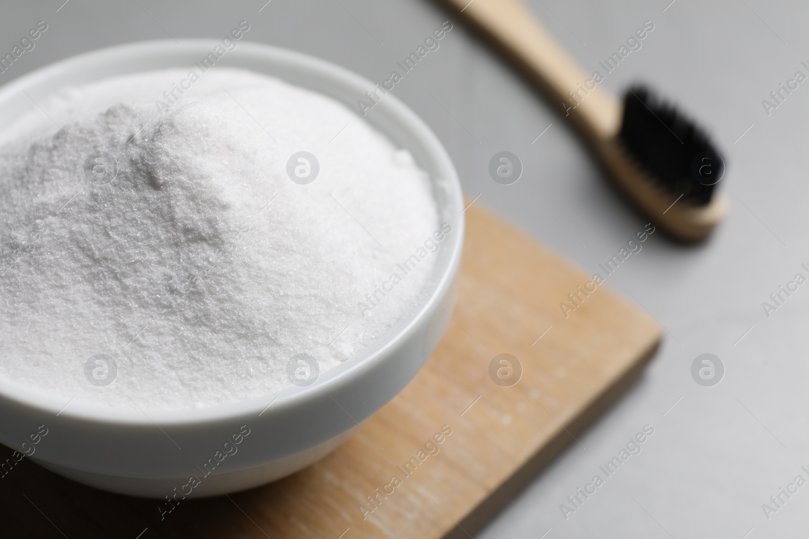 Photo of Bamboo toothbrush and bowl of baking soda on grey table, closeup. Space for text