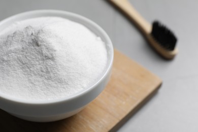 Bamboo toothbrush and bowl of baking soda on grey table, closeup. Space for text