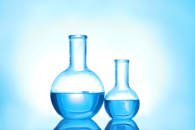 Photo of Laboratory glassware with liquid on color background. Solution chemistry
