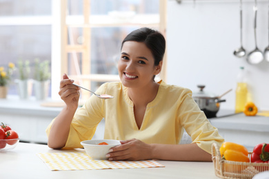 Photo of Young woman eating tasty vegetable soup at table in kitchen