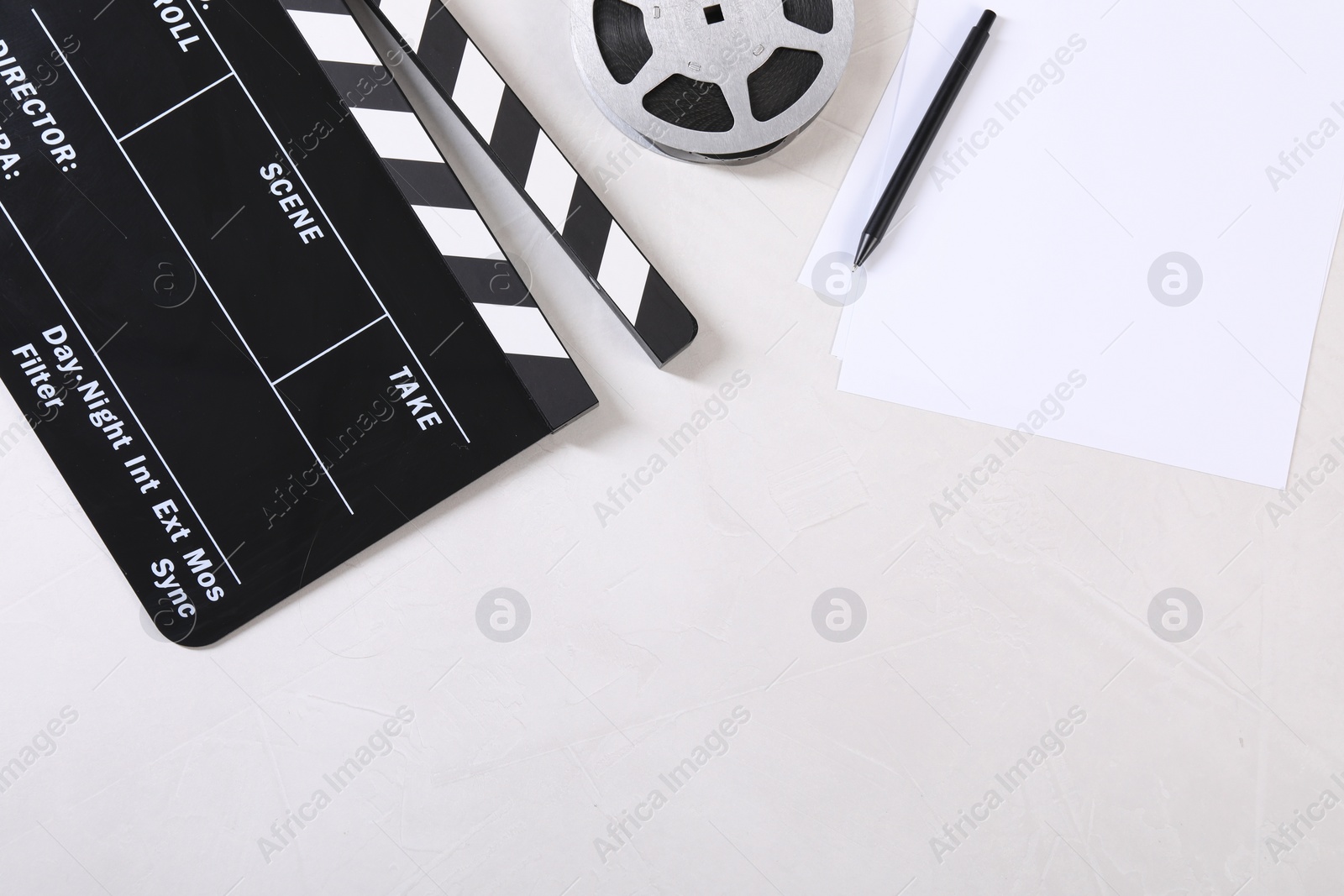 Photo of Movie clapper, film reel, sheets and pen on light textured table, flat lay. Space for text