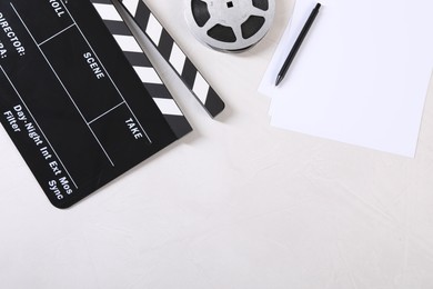 Movie clapper, film reel, sheets and pen on light textured table, flat lay. Space for text