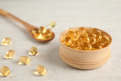 Bowl and spoon with cod liver oil pills on light background