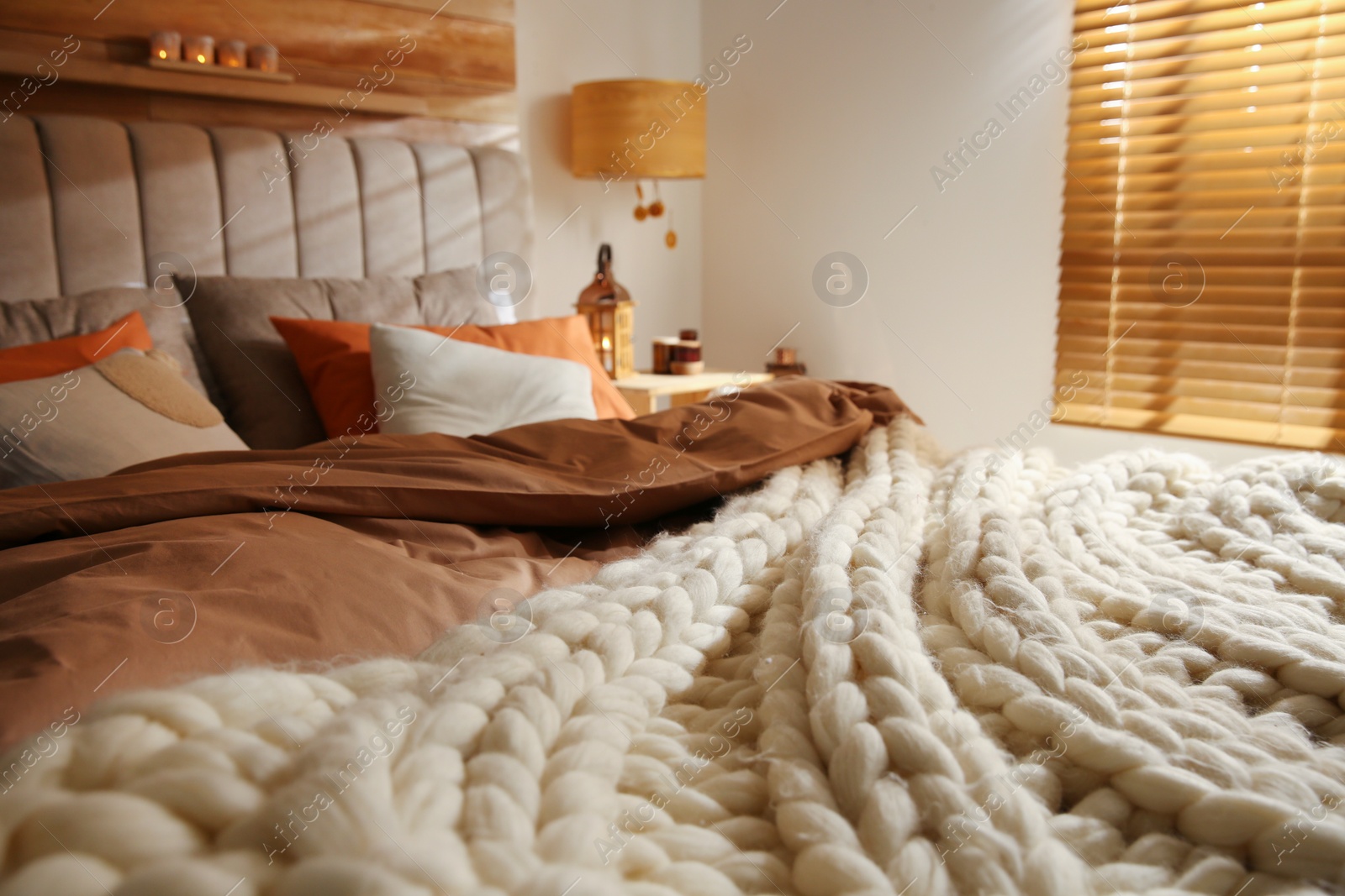 Photo of Bed with cozy knitted blanket and cushions indoors. Interior design