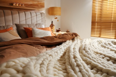 Photo of Bed with cozy knitted blanket and cushions indoors. Interior design