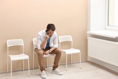 Photo of Man talking on smartphone and waiting for appointment indoors