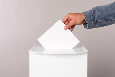 Photo of Man putting his vote into ballot box on light grey background, closeup