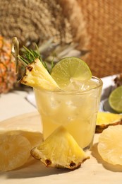 Glass of tasty pineapple cocktail and sliced fruits on table