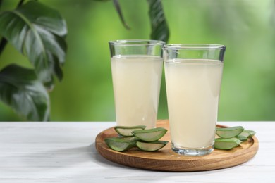 Photo of Fresh aloe juice in glasses and cut leaves on white wooden table outdoors. Space for text