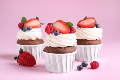 Photo of Delicious cupcakes with cream and berries on pink background