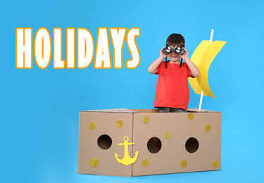 School holidays. Cute little child playing with cardboard ship near blue wall. Banner design 