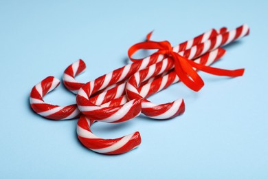 Photo of Sweet Christmas candy canes with red bow on light blue background, closeup