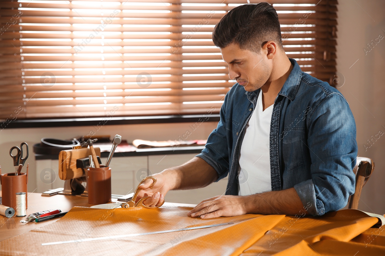 Photo of Man cutting leather with scissors in workshop