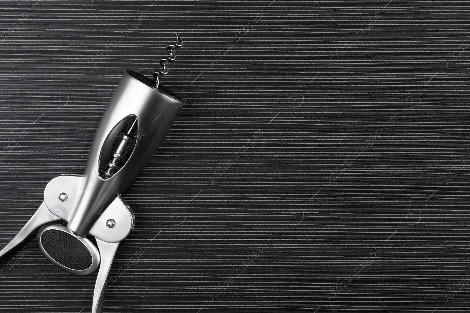 Photo of One wing corkscrew on black wooden table, top view. Space for text