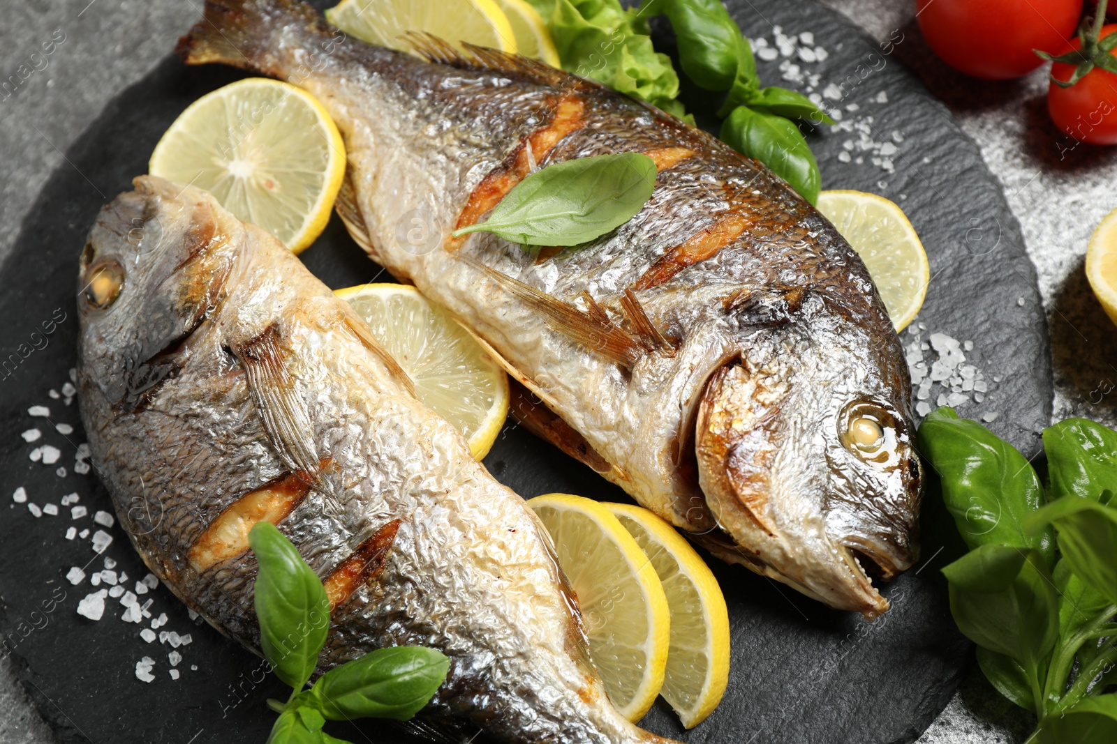 Photo of Delicious roasted fish with lemon on slate plate, closeup