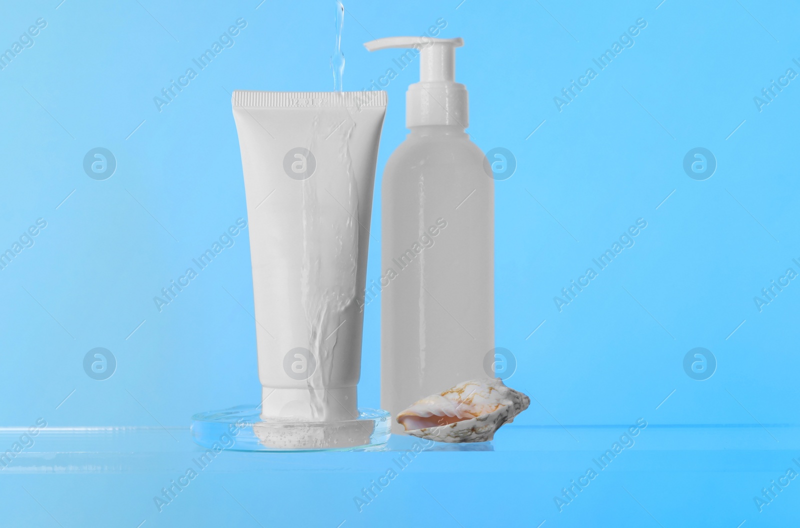 Photo of Pouring water on face cleansing products, petri dish and seashell against light blue background