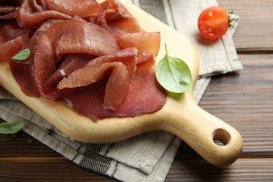 Photo of Board with delicious bresaola on wooden table, closeup